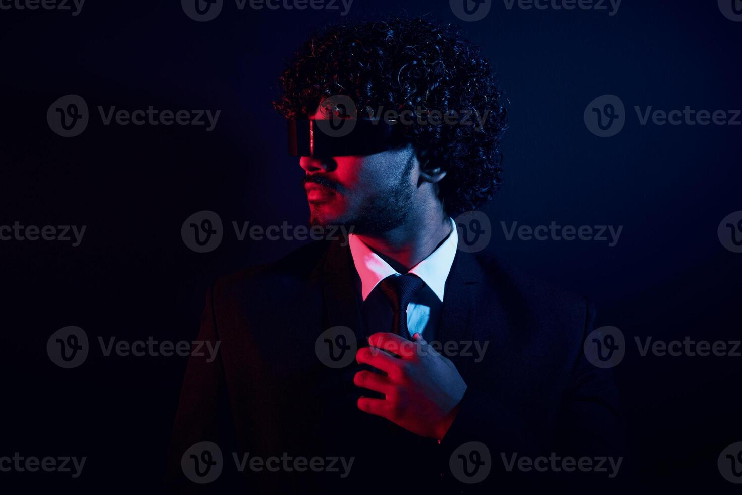 Confident businessman in futuristic glasses adjusting his necktie against black background photo