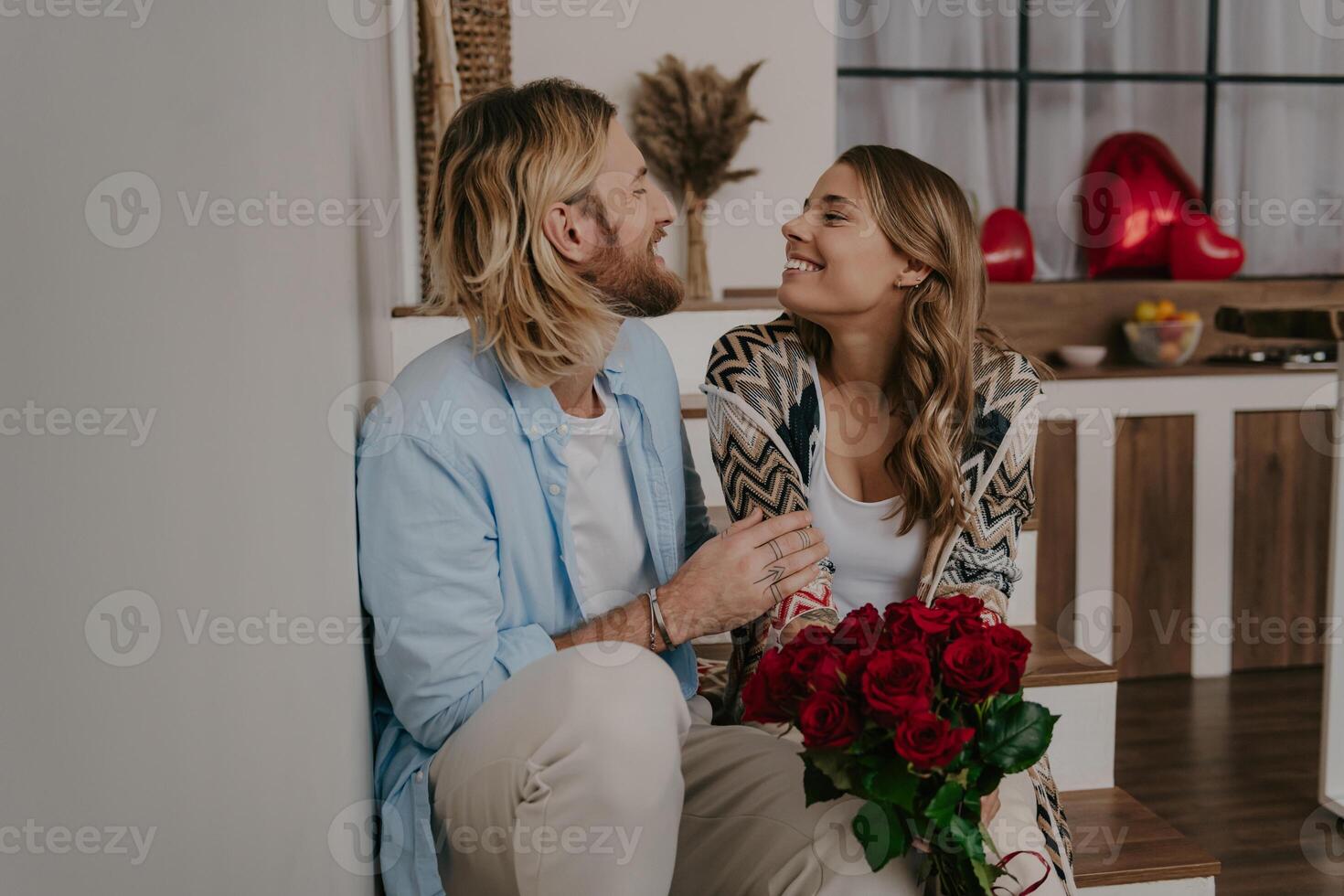 Young loving couple embracing and holding flower bouquet while celebrating anniversary at home photo