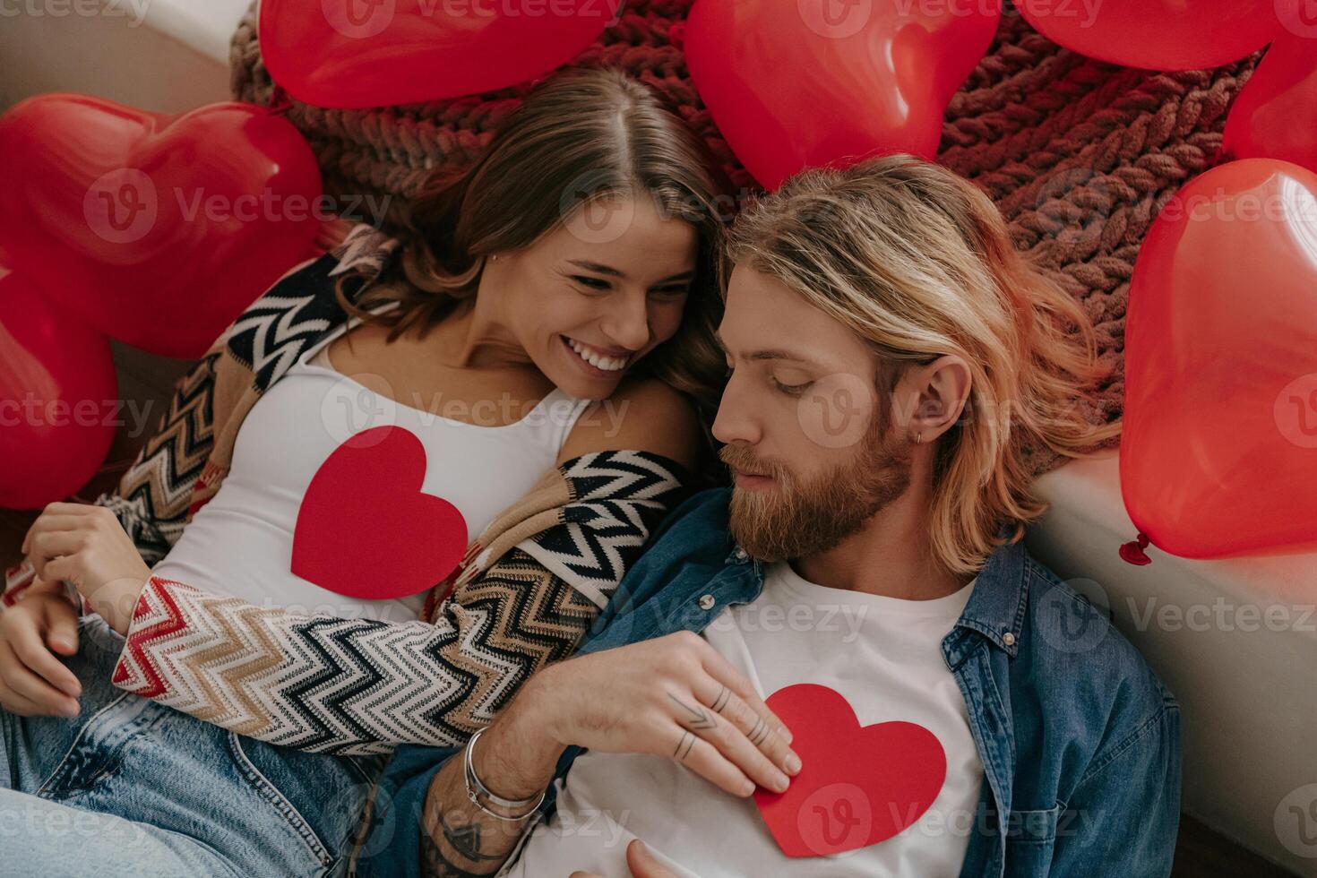 Top view of romantic couple holding heart shape Valentine cards while lying on bed surrounded with red balloons photo