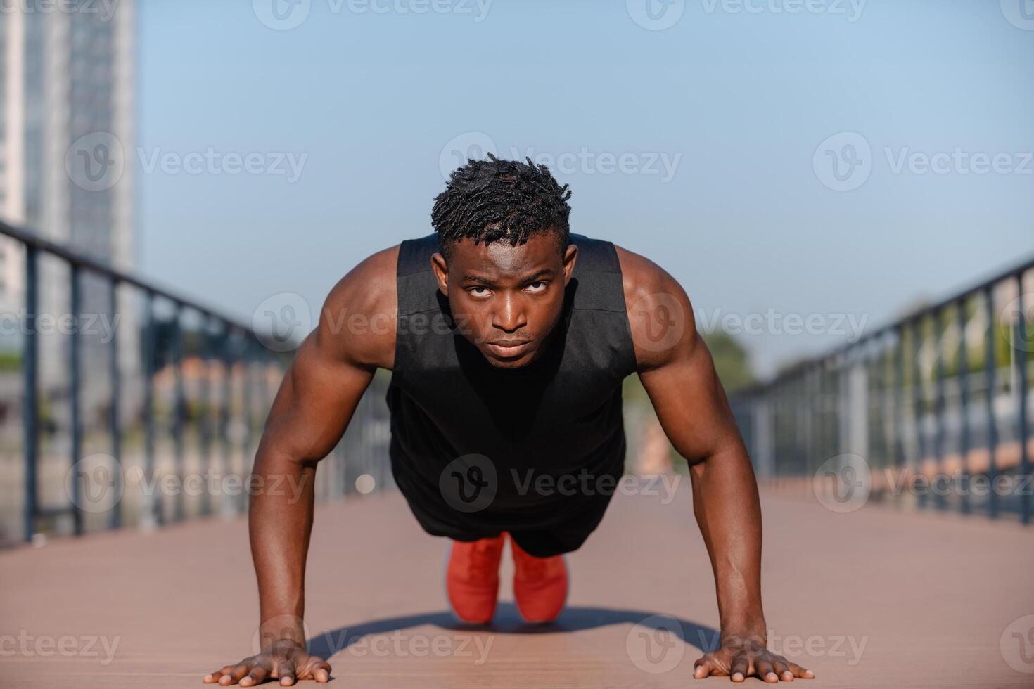 Confident young African athlete in sportswear doing push-ups while exercising outdoors photo