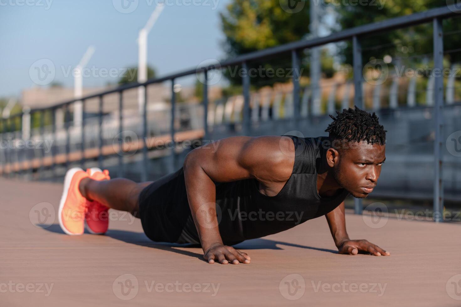 Confident African man in sportswear doing push-ups while exercising outdoors photo