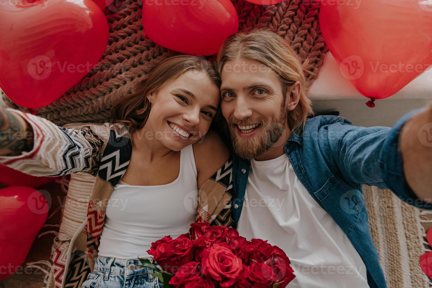 Top view of happy loving couple holding flowers and making selfie with red heart shape balloons around them photo