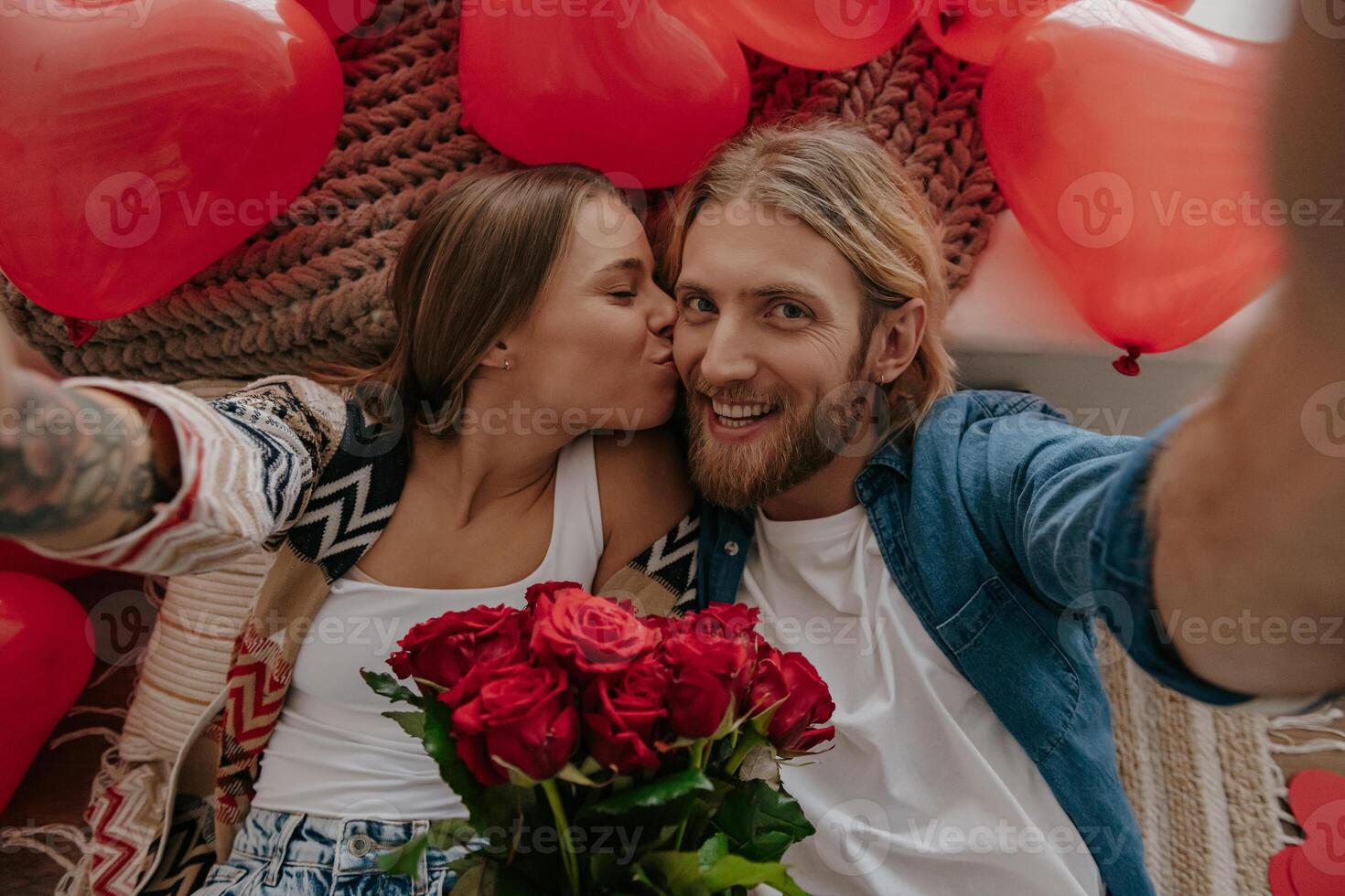 Top view of happy loving couple kissing and making selfie with red heart shape balloons around them photo