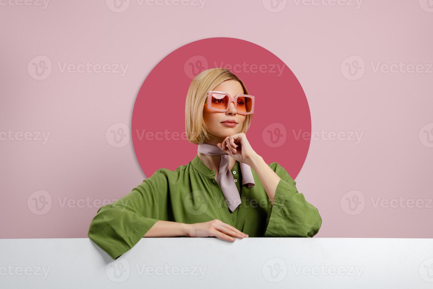 Fashionable young woman in trendy eyeglasses leaning at copy space against pink background photo