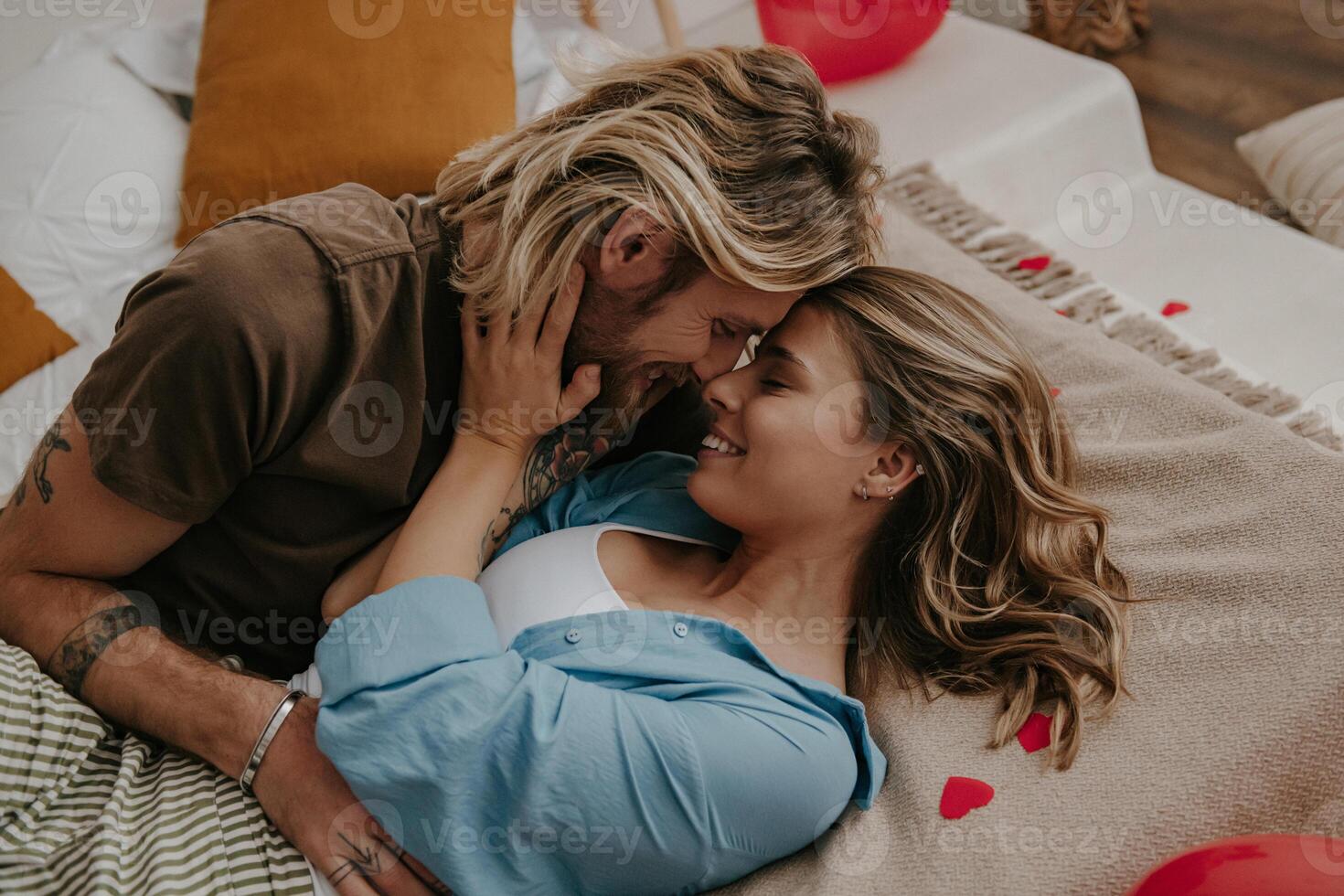 Young loving couple embracing and kissing while lying in bed surrounded with red heart shape balloons photo