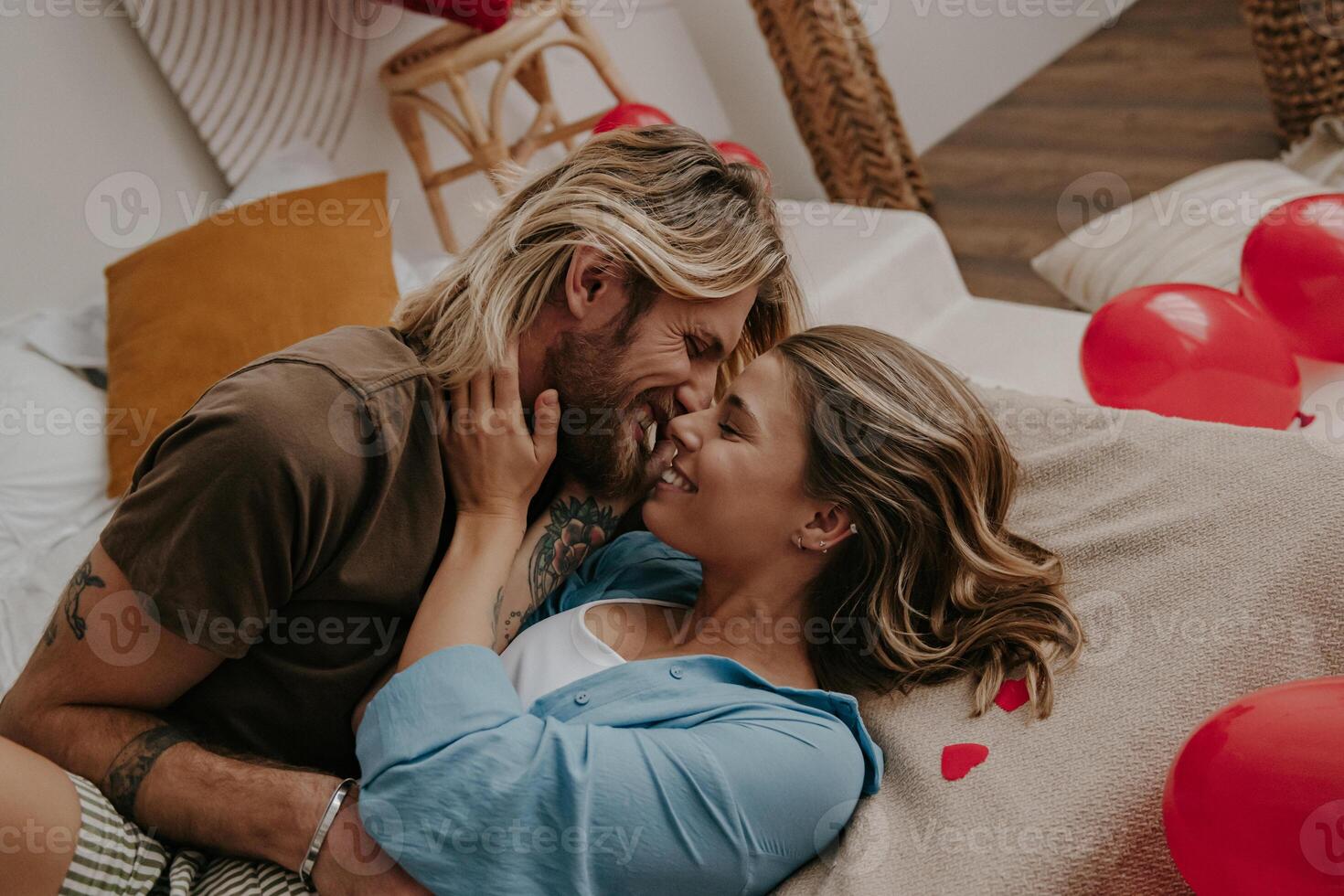 Young loving couple embracing and kissing while lying in bed surrounded with red heart shape balloons photo
