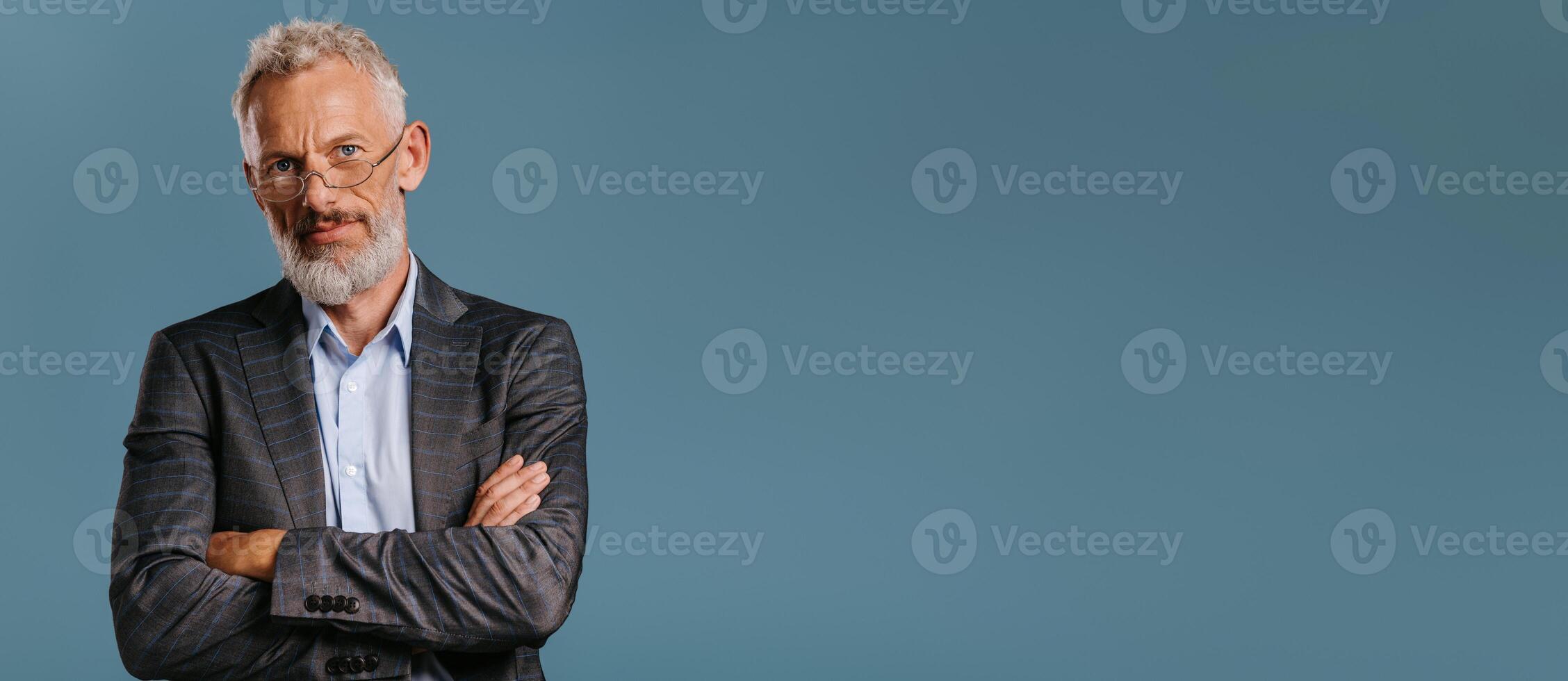 Confident mature businessman keeping arms crossed while standing on colored background photo