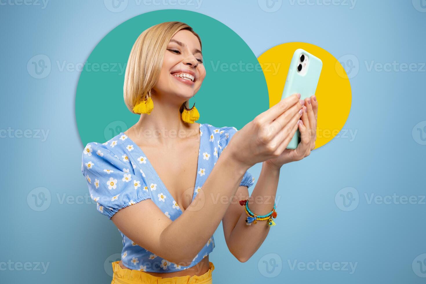 Beautiful young woman using smart phone and smiling against blue background photo
