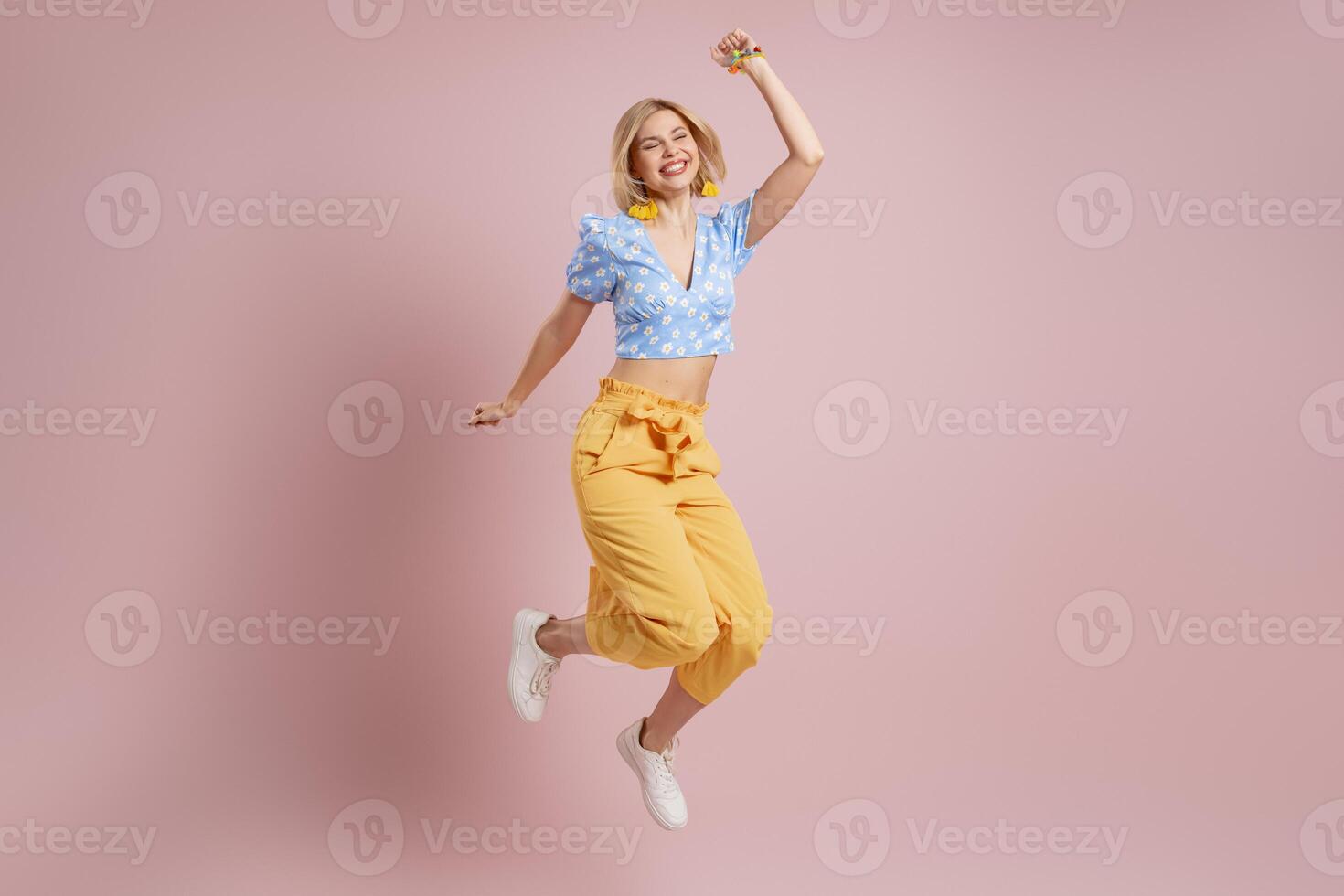 Full length of excited young woman jumping and smiling against pink background photo