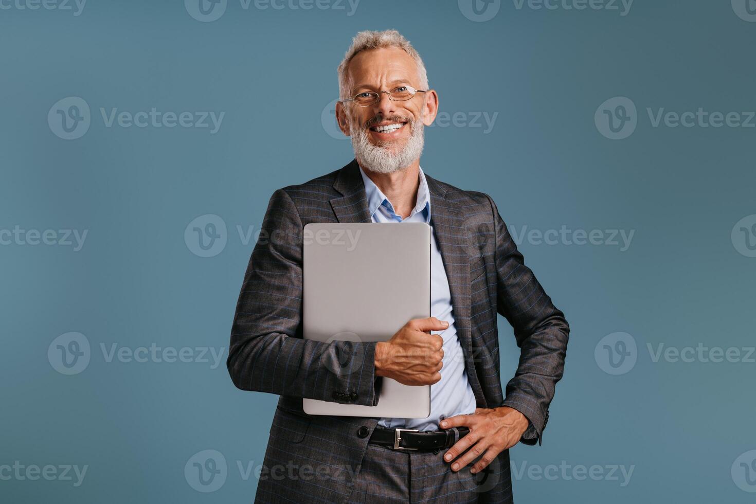 Confident mature businessman in suit carrying laptop while standing on colored background photo
