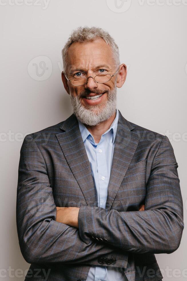 Confident mature businessman in formalwear keeping arms crossed and smiling against white background photo