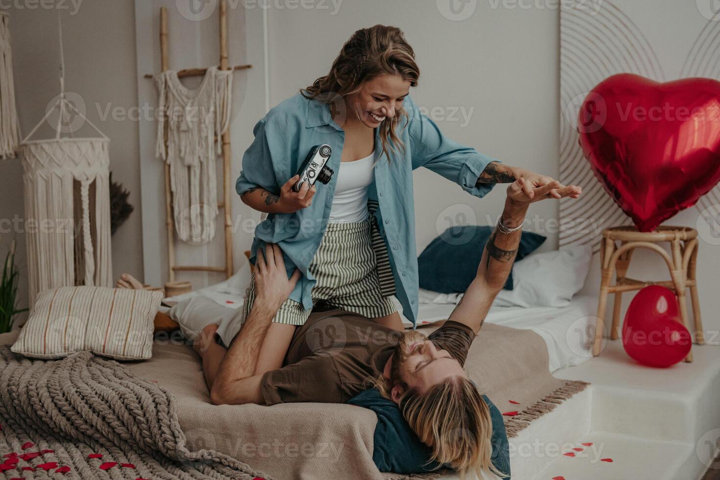 Playful young woman photographing her boyfriend with retro camera while relaxing in bed at home together photo
