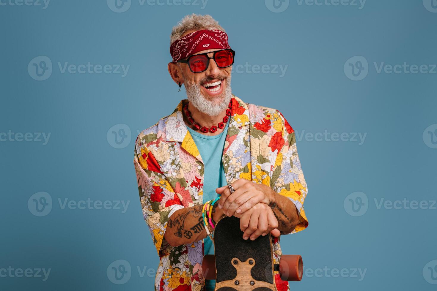 Happy mature man in funky shirt leaning on longboard and smiling against blue background photo