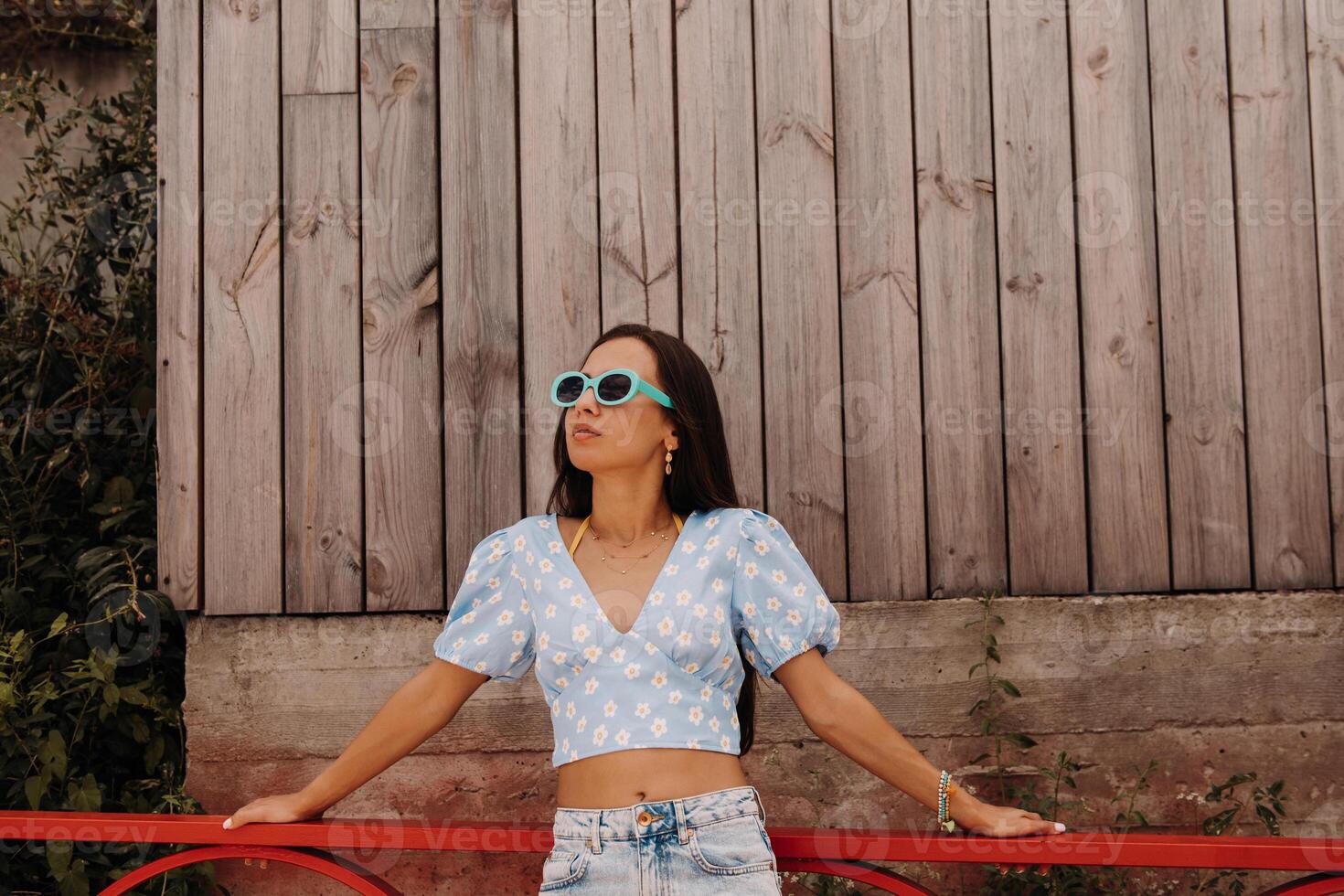 Fashionable young women in trendy glasses standing against wooden wall outdoors photo