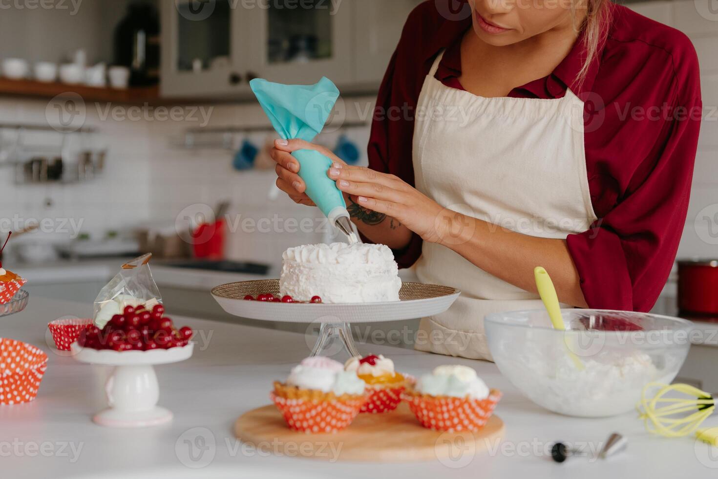 Close-up of skilled female pastry chef applying whipped cream while decorating cake at the kitchen photo
