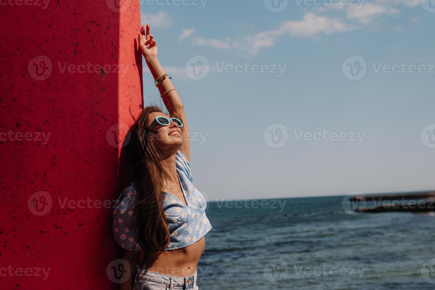 Happy young woman looking relaxed while leaning on the colorful wall with the sea on background photo