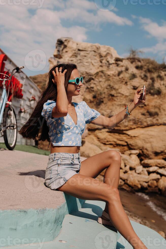 Attractive young woman using smart phone and smiling while sitting seaside photo
