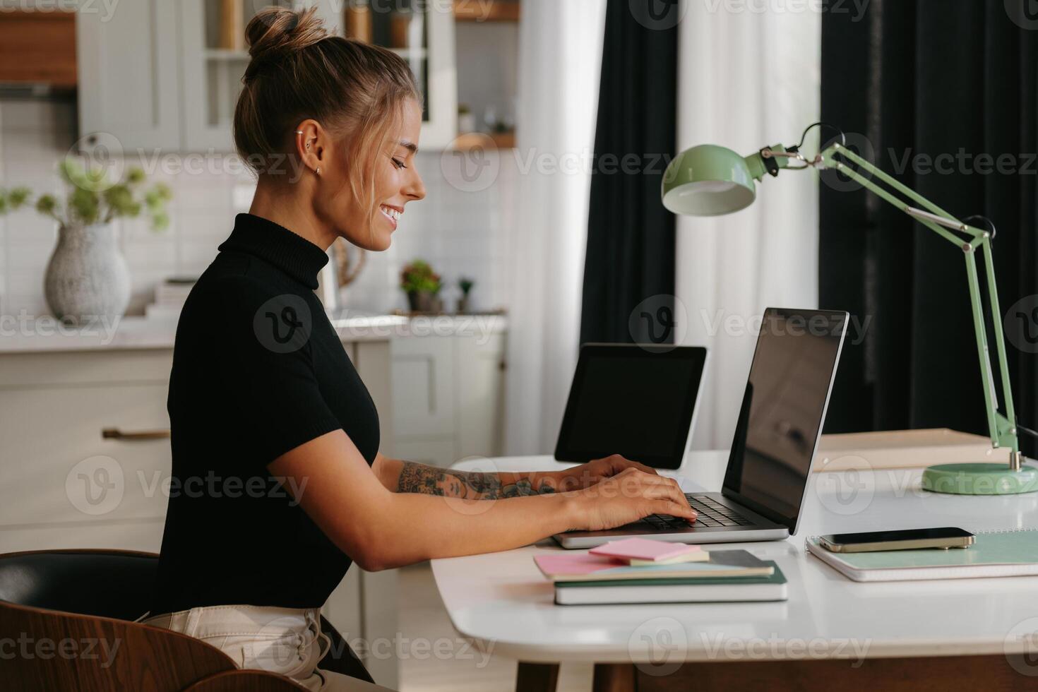 Side view of smiling young woman sitting at the desk and using laptop while working at home photo