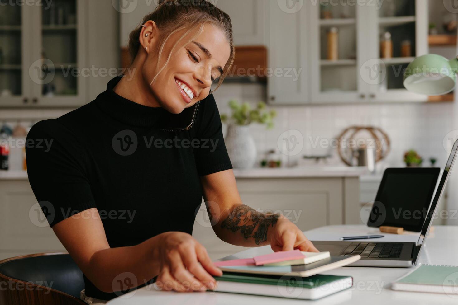 Busy young woman talking on mobile phone and smiling while working at home photo