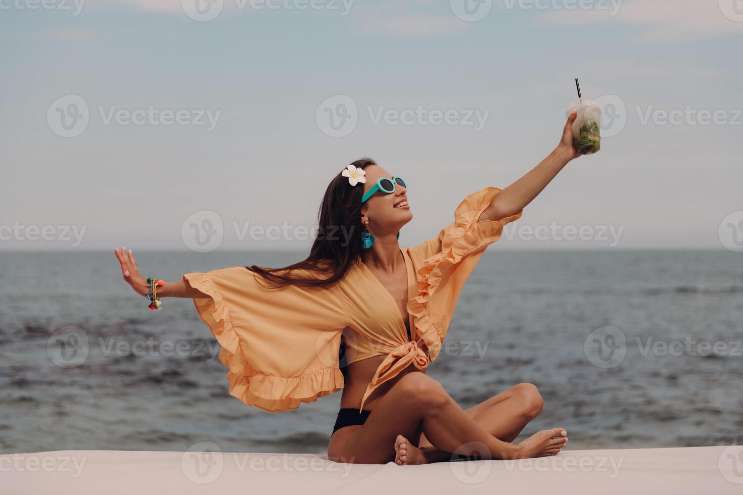 Happy young woman in boho styled crop top enjoying cocktail while relaxing seaside photo