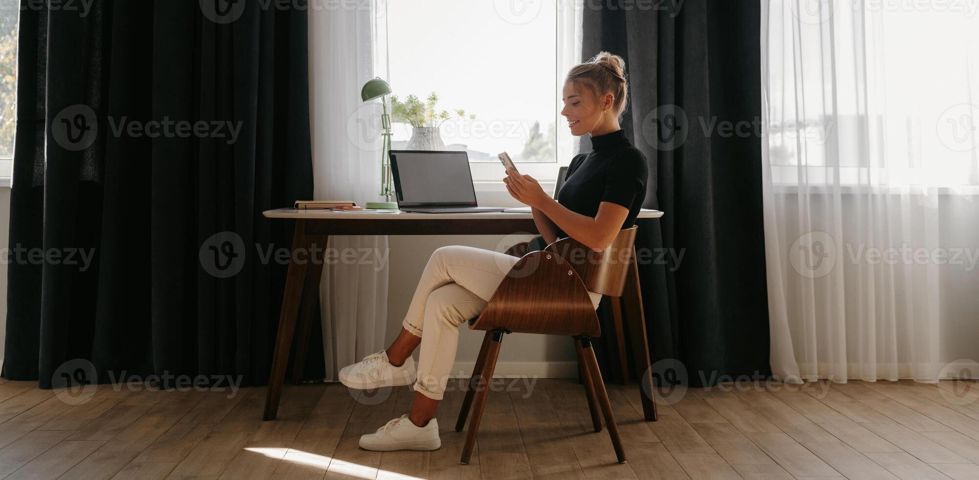 Confident young businesswoman using smart phone while working at home front of the window photo