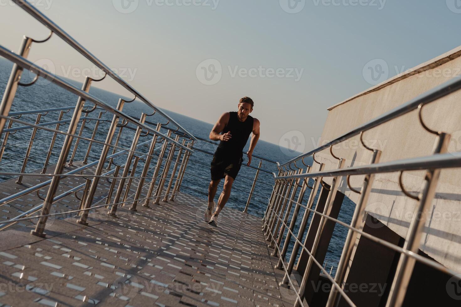 Confident young man in sports clothing enjoying early morning jog with the sea on background photo