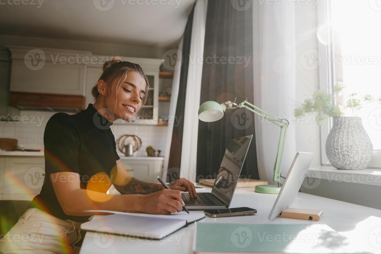 Confident young woman making notes in her note pad and smiling while working at home photo