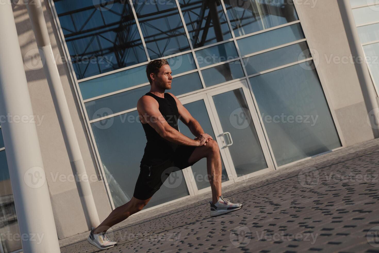 Confidant male athlete doing stretching exercises outdoors against urban building photo