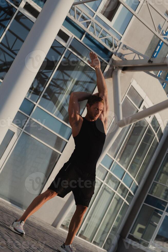 Handsome muscular man in sports clothing doing stretching exercises outdoors at early morning photo