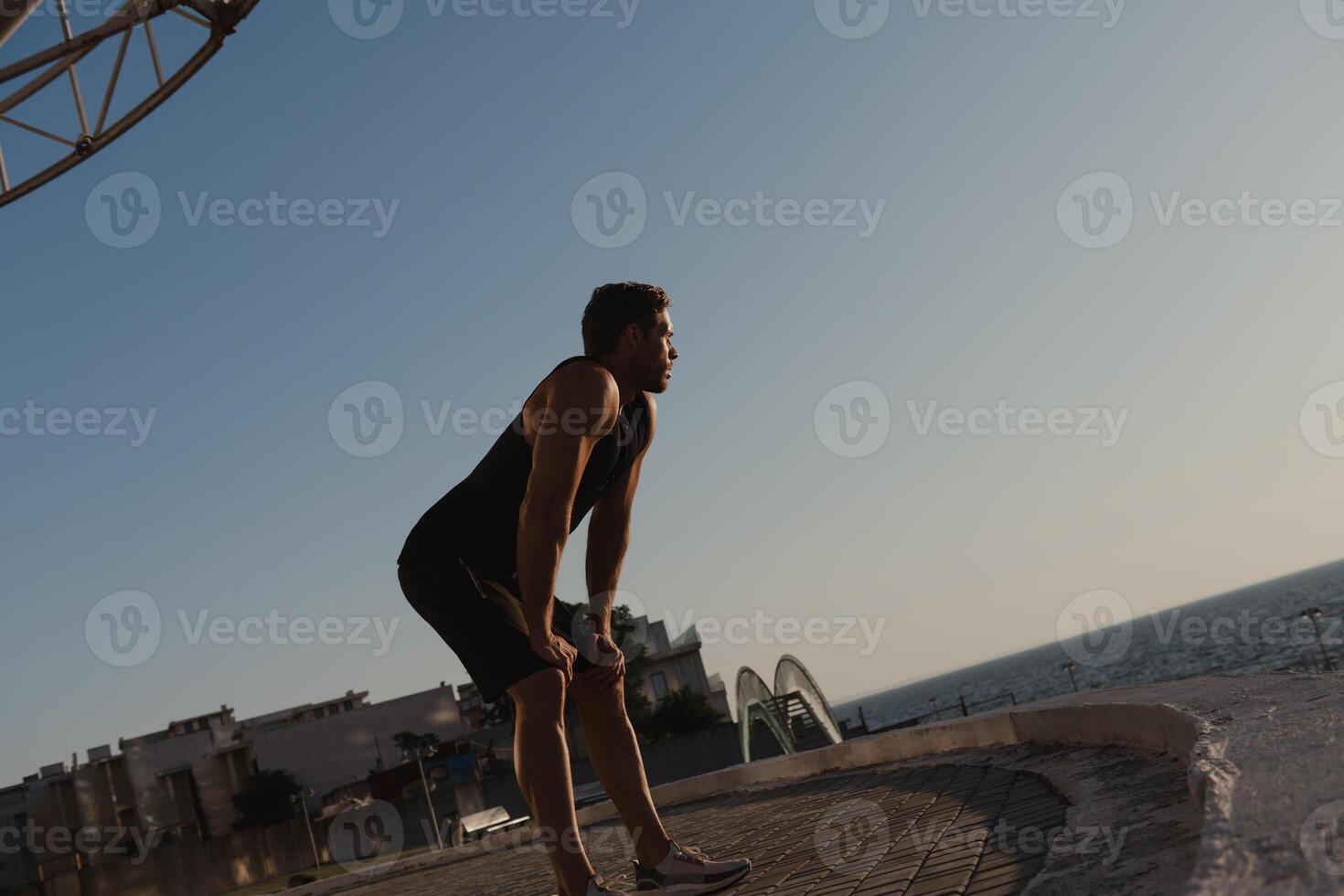 Tired male athlete enjoying sea view while relaxing after morning sport training outdoors photo