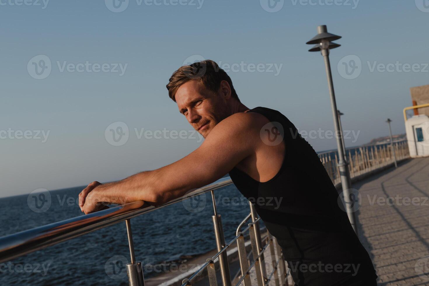 Tired male athlete enjoying sea view while relaxing after morning sport training outdoors photo