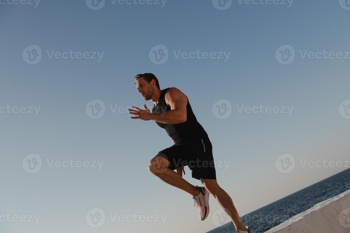 Strong young man in sports clothing exercising outdoors with sea on the background photo