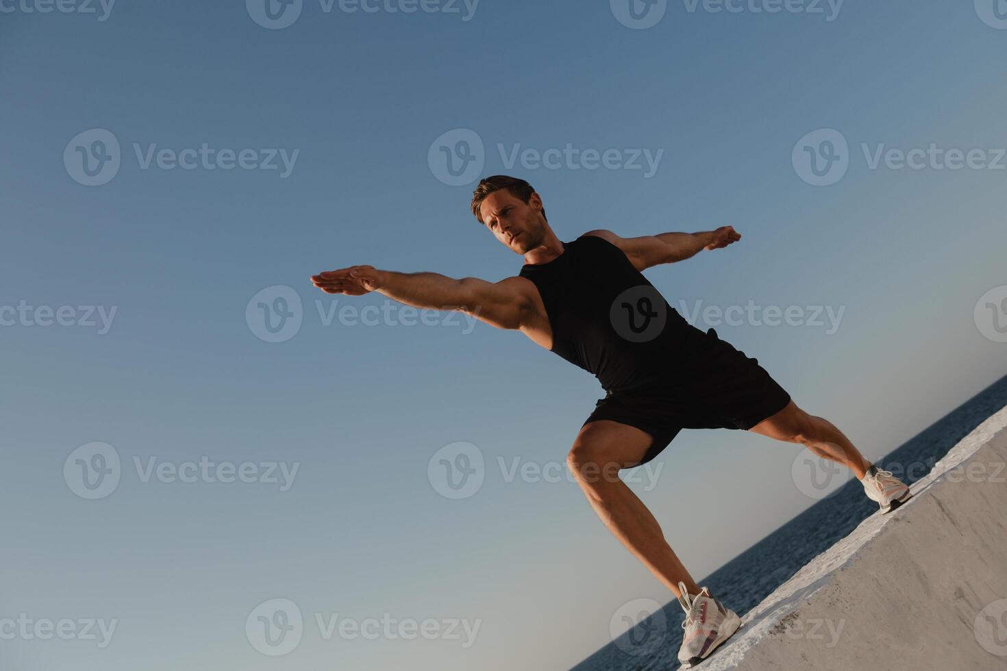 Low angle view of young male athlete doing stretching exercises with the sea view on background photo