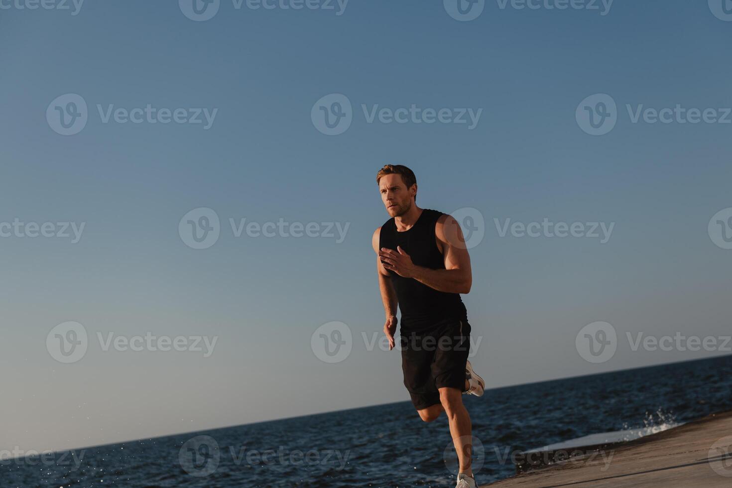 Confident athletic man in sports clothing running outdoors with the sea on background photo