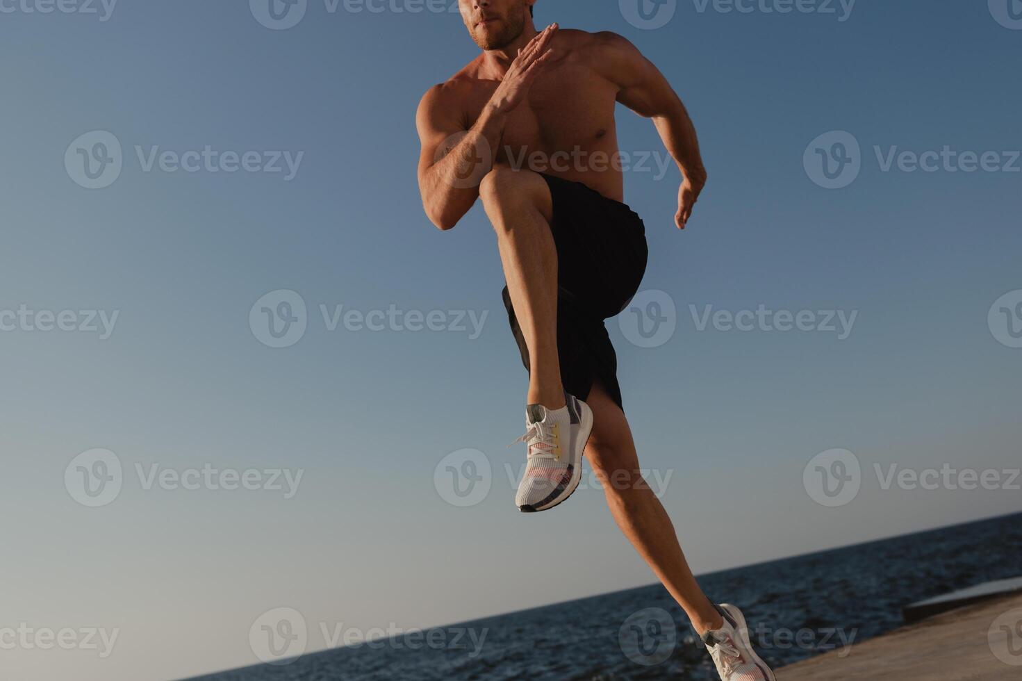 Close-up of unrecognizable young male athlete jumping outdoors with the sea on background photo