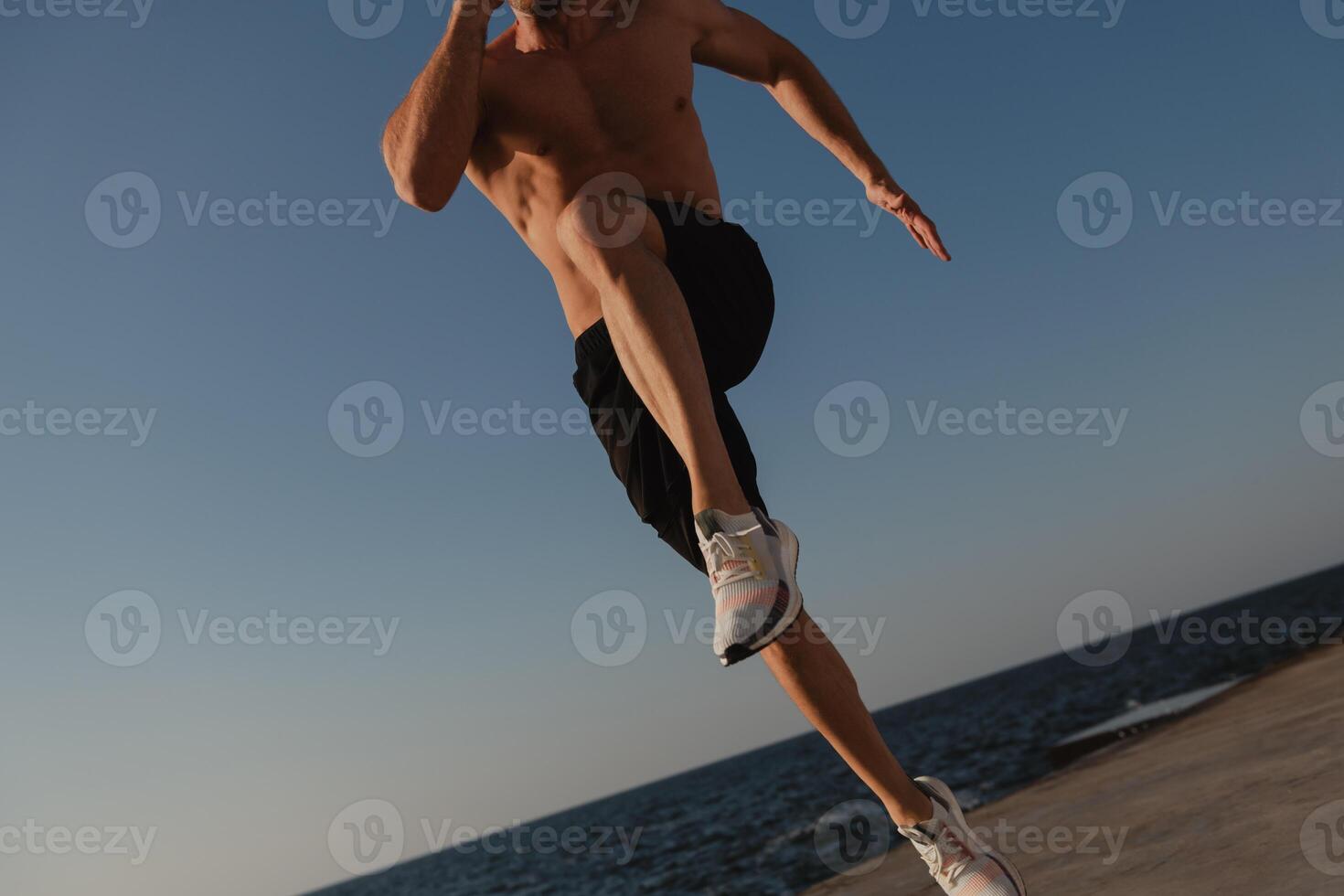 Close-up of unrecognizable muscular man jumping outdoors with the sea on a background photo