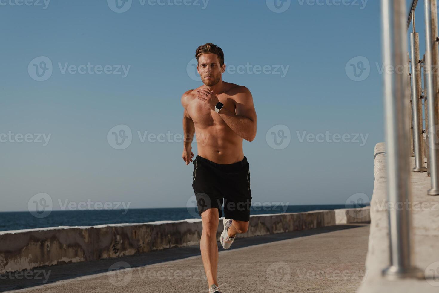 Handsome male athlete running by the pier with the sea on background photo