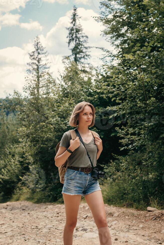Beautiful young female traveler with backpack walking by the mountain footpath photo