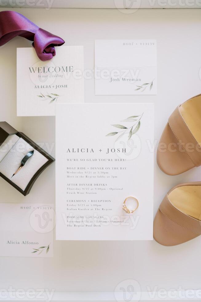 Wedding rings in a box next to invitations, bridal shoes and groom tie photo