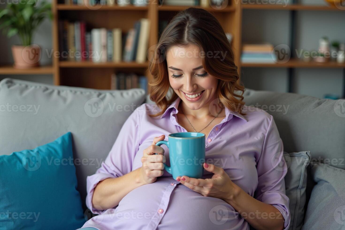 photo of pregnant woman sit on couch both hands holding cup of coffee,