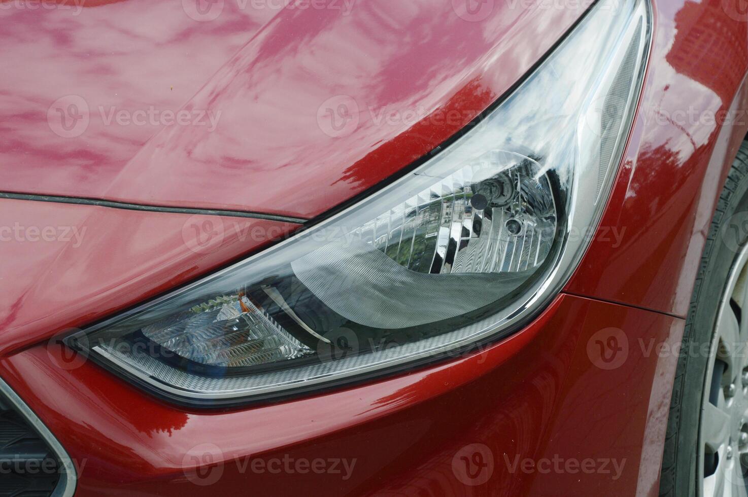 Front headlight and part of the hood of a modern red passenger car. photo
