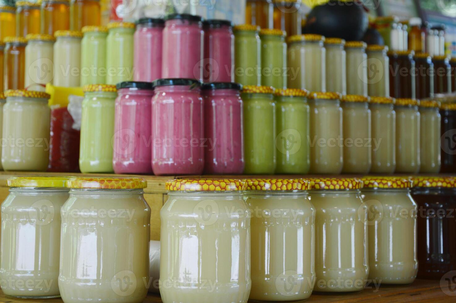 Rows of various jars of honey and berry jam on wooden shelves in a market stall. Seasonal harvest. Canned goods. photo