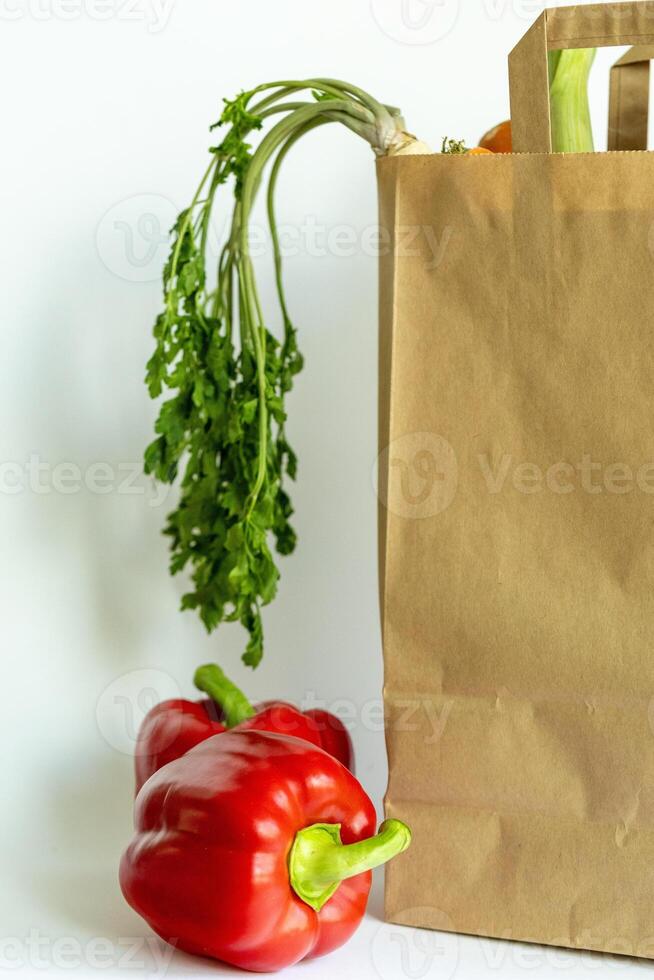 Kraft paper bag filled with fresh vegetables and bread, on white background, fresh vegetable delivery and shopping at local markets, farm produce photo