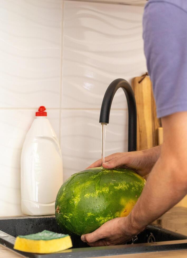 man washing watermelon in kitchen under running water, healthy eating and hygiene photo