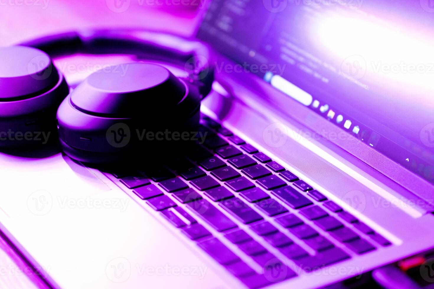 modern wireless headphones and laptop with software code on screen in neon purple light, suitable for software development , IT education topics photo