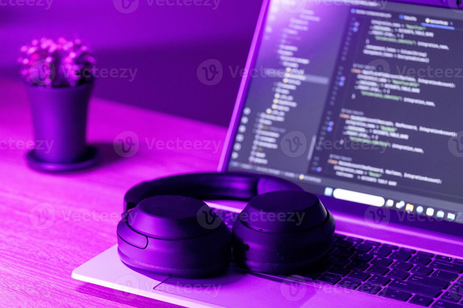 modern wireless headphones and laptop with software code on screen in neon purple light, suitable for software development , IT education topics photo