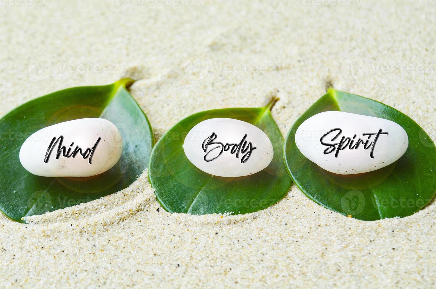 Mind, Body and Spirit text engraved on white zen stones with leaf and sand background. Mind, Body and Spirit concept photo
