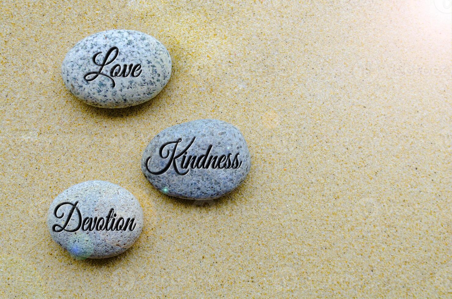 Top view of Love, Kindness and Devotion Joy text engraved on stones with beach sand background. photo