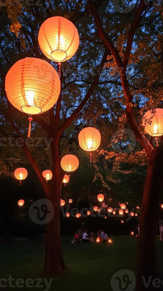 Brightly lit Chinese lanterns hang from trees in night garden. Mid-Autumn festival. Vertical banner photo