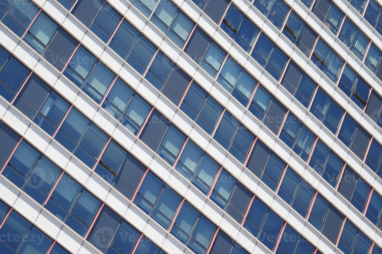 A modern office building facade with slanted glass windows reflecting the cityscape photo